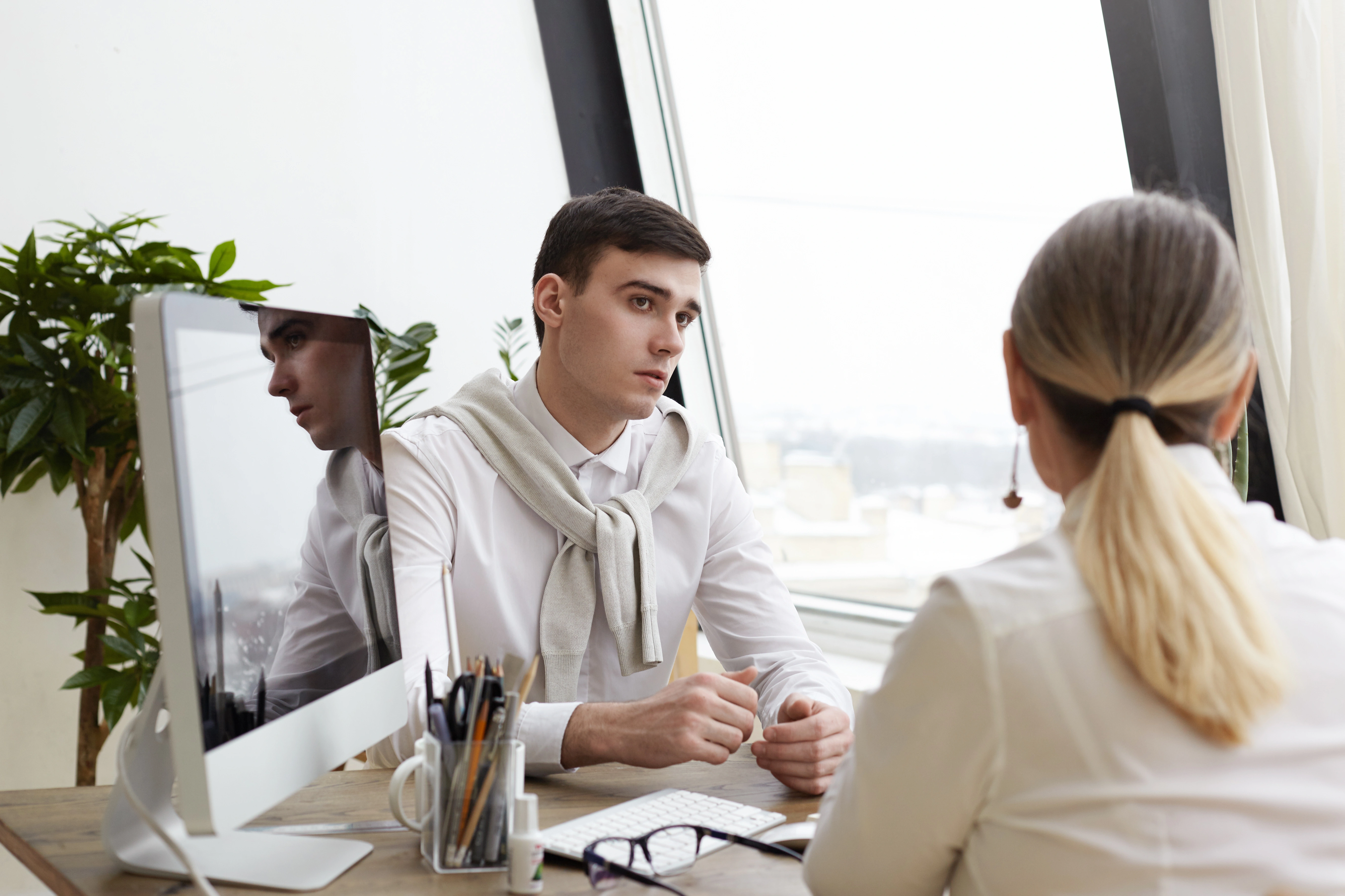 Мужчина и женщина беседуют за рабочим столом с компьютером в светлом офисе.